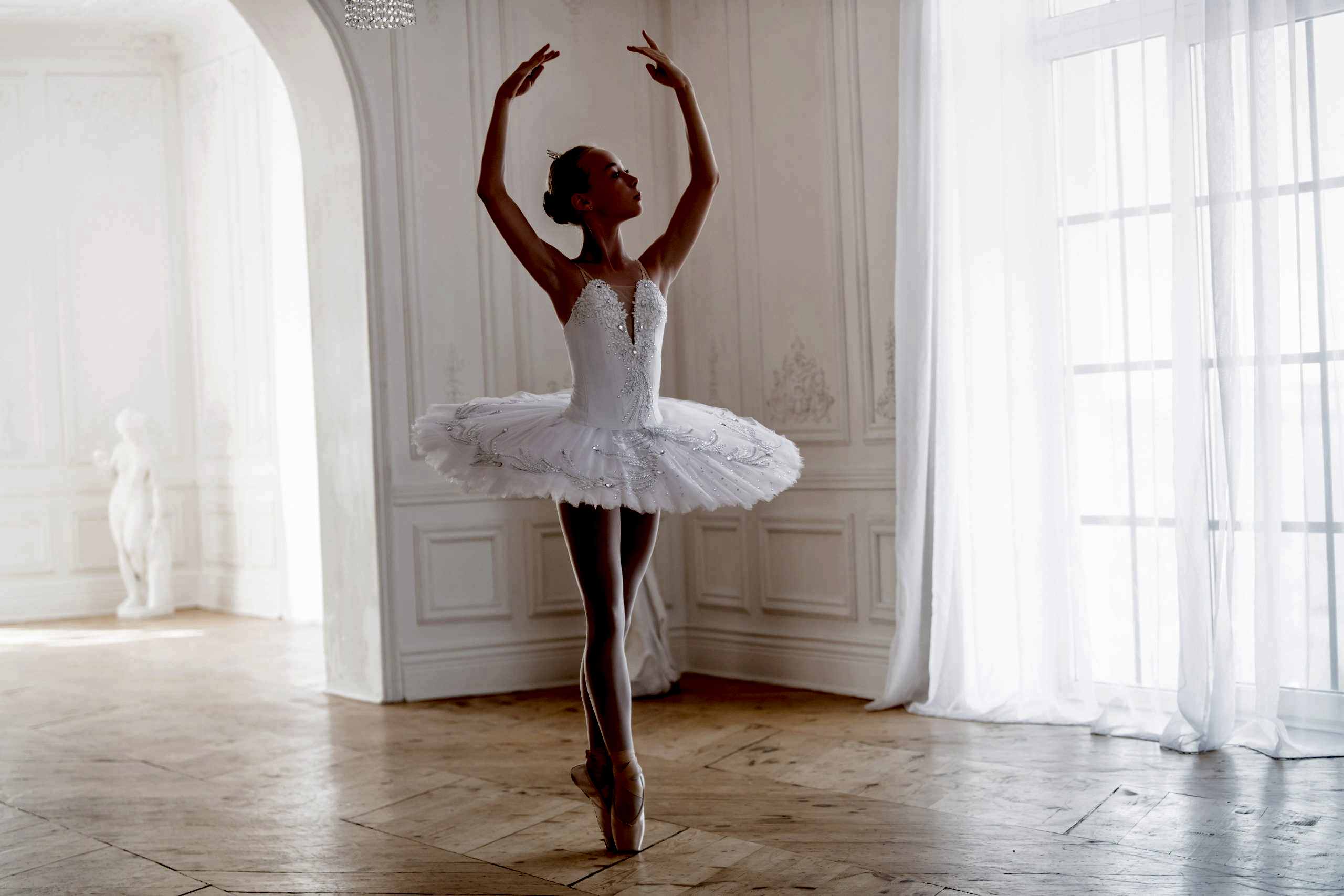 young slender ballerina in a white tutu in pointe shoes is dancing in large beautiful white hall.